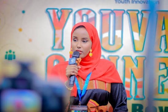 Speaker holding a microphone in front of the YouVate Connect 2026 backdrop